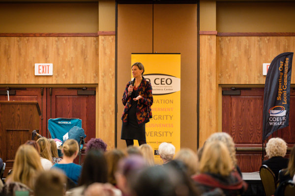 A woman stands on stage speaking into a microphone at a women's business conference.