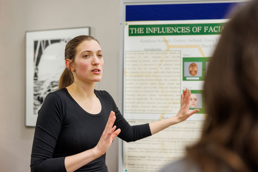 a woman presents her research poster at the annual symposium