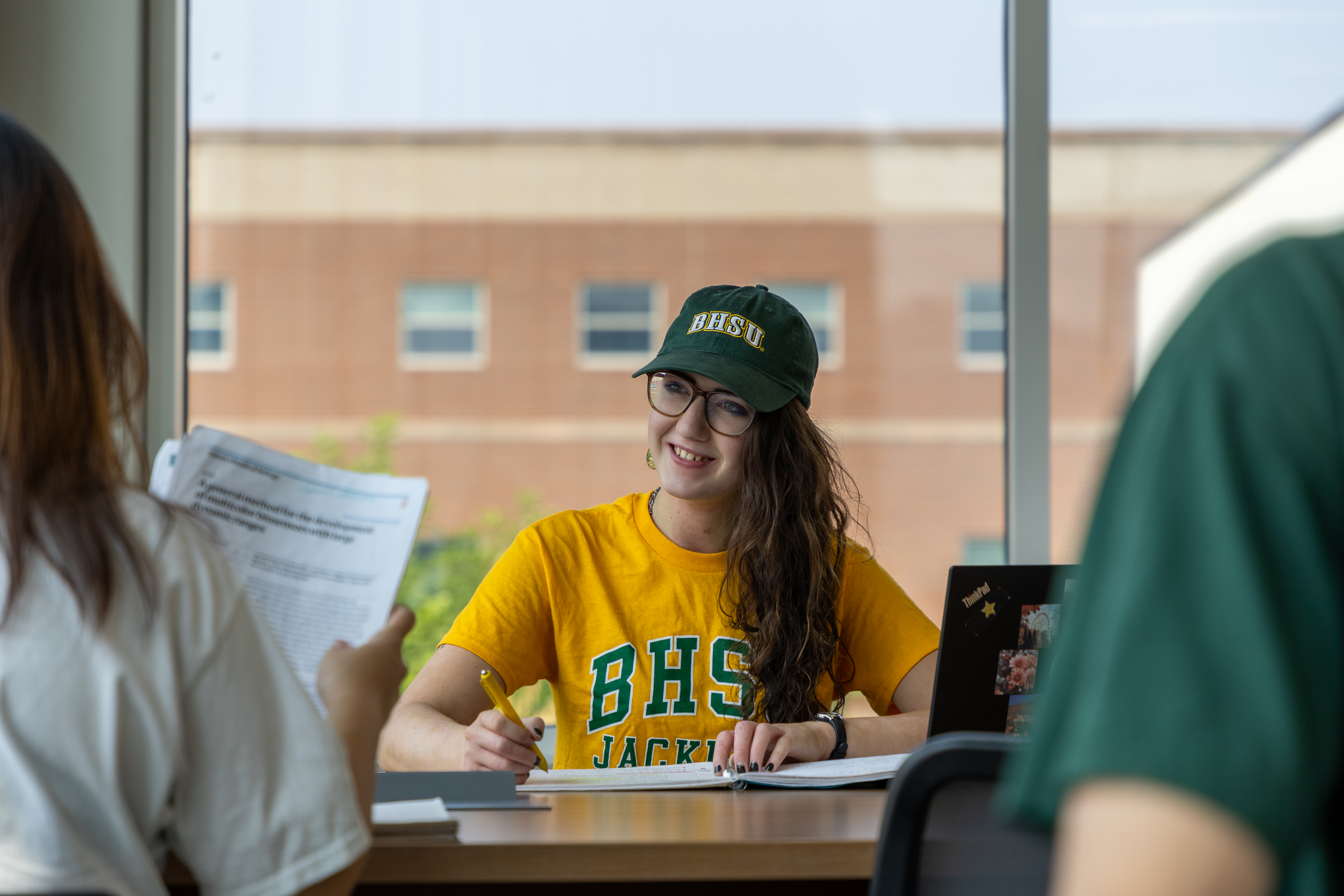A BHSU Applied Science student sits in the library with two other students sitting across from her.
