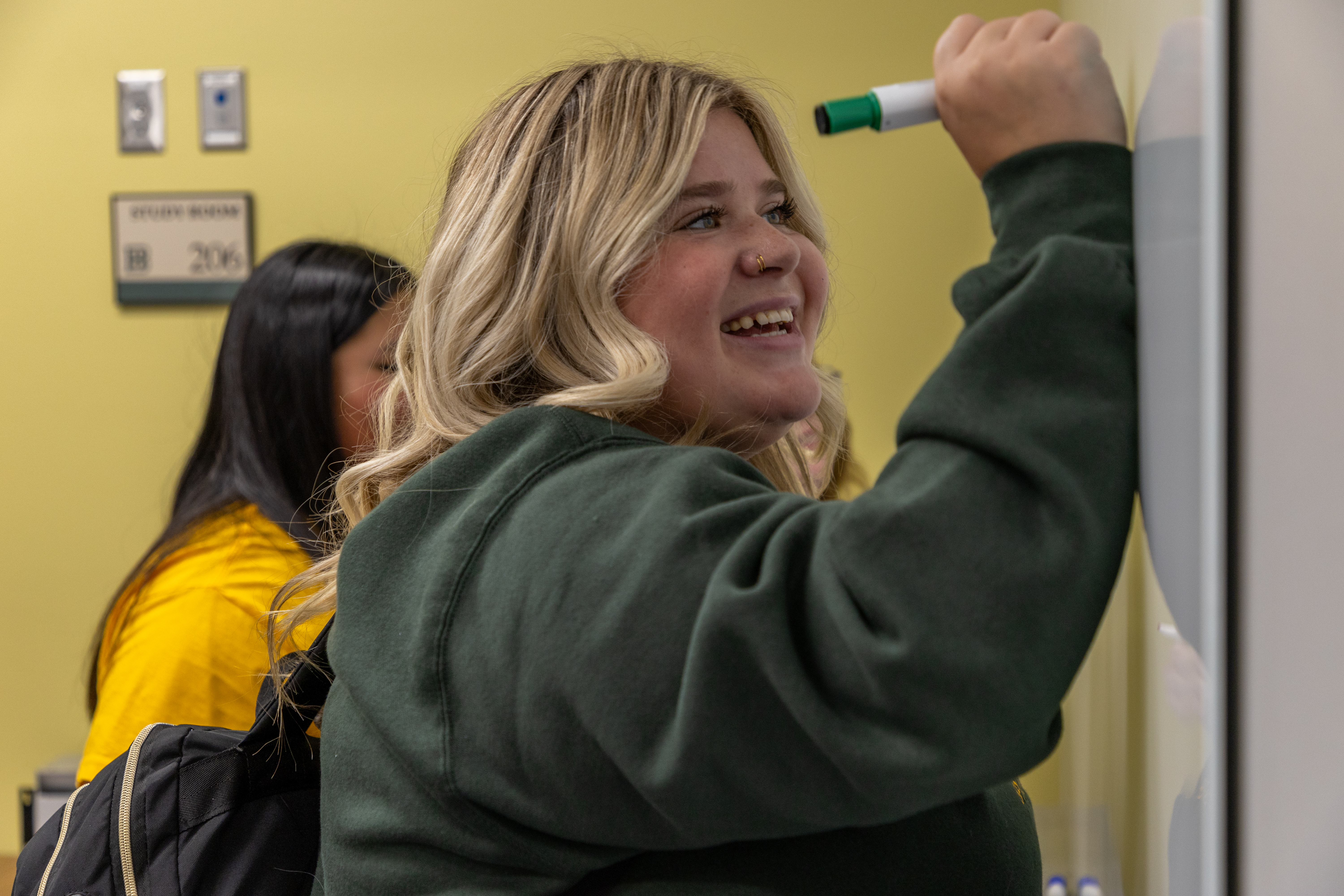 A female BHSU student takes notes on a whiteboard in a study room in the library.