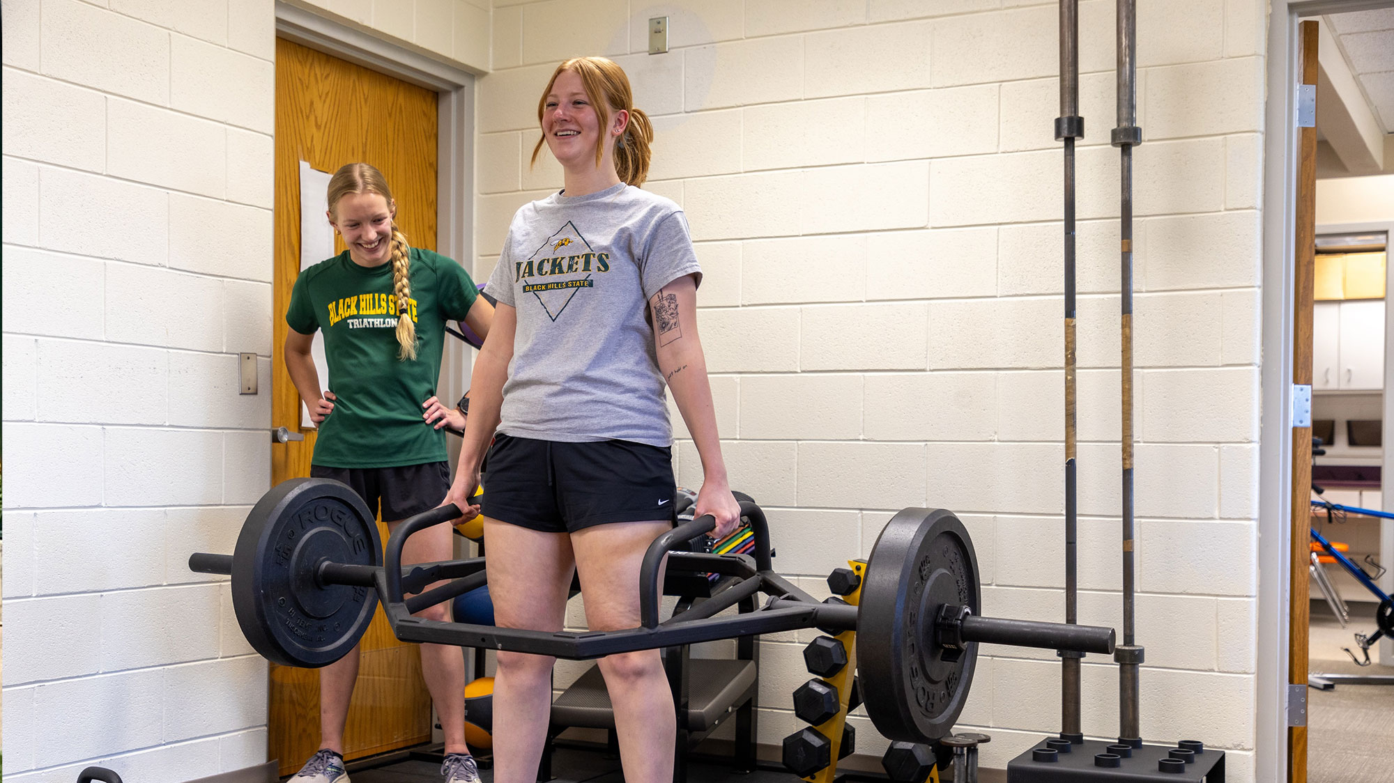 Image of two BHSU exercise science majors with weight lifting equipment in a classroom. Both students are smiling.