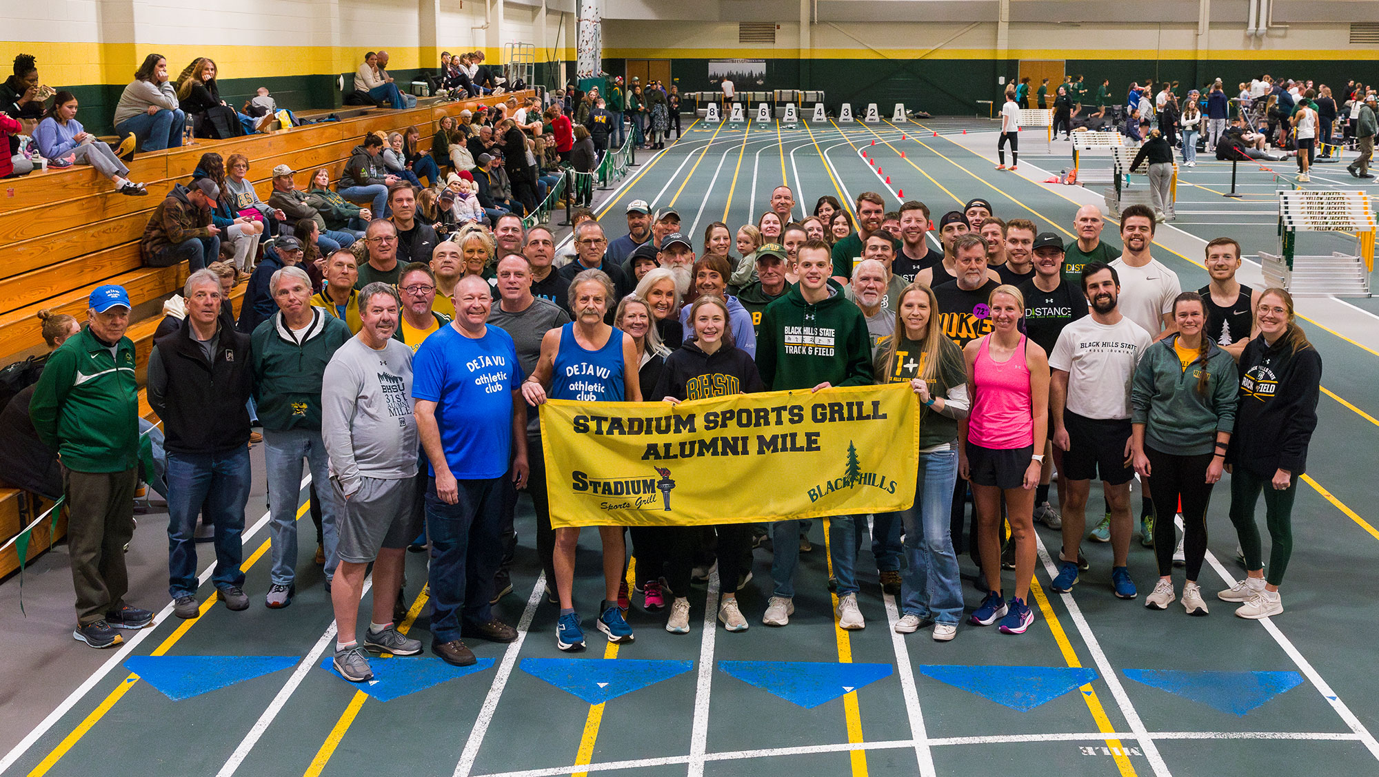 Group of runners at the 2025 BHSU Alumni Mile posing with a 'Stadium Sports Grill Alumni Mile' banner.