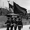 Four ROTC members marching, two holding guns and two holding a flag.